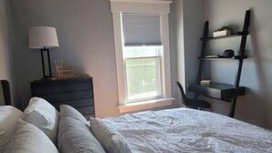 Une chambre à coucher comprenant un lit, une table de chevet, une lampe, une fenêtre et une étagère avec divers objets.