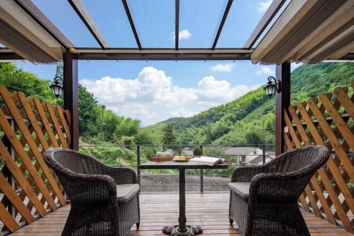 Un área de estar al aire libre con techo, con sillas de mimbre y una mesa, con vistas a un valle verde y exuberante.