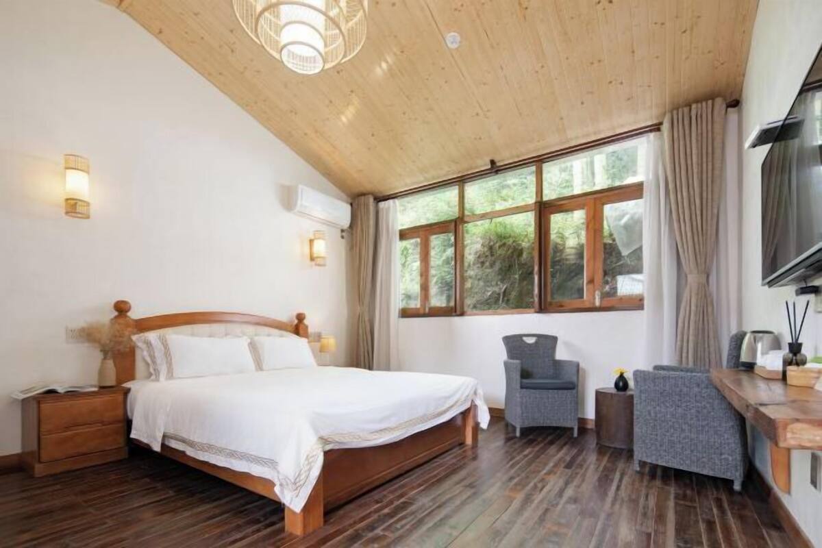 Un dormitorio con techo de madera, cama, escritorio, silla y televisor.