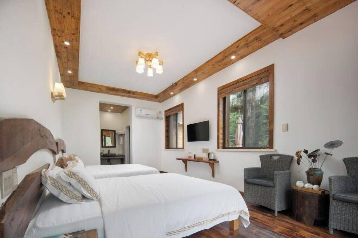 Un dormitorio con dos camas, vigas de madera en el techo, un televisor, una ventana y una pequeña mesa con sillas.