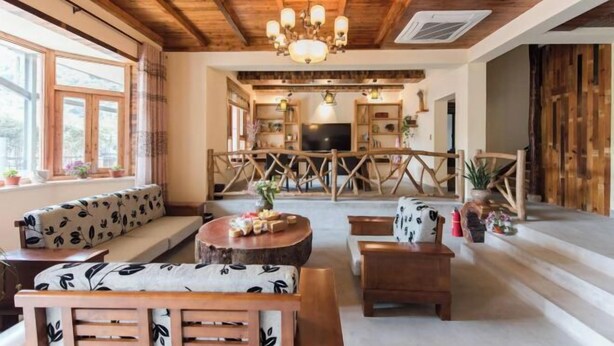 A cozy room with a wooden ceiling, a sofa with a leaf pattern, a round wooden table, and a TV in the background. - Moganshan Xiyuan Inn (Deqing)