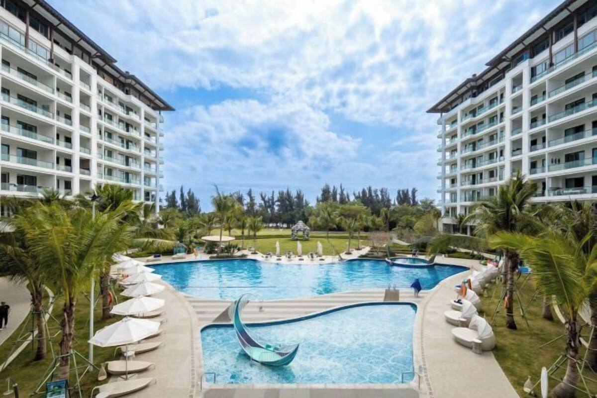 Un hôtel doté d’une grande piscine entourée de palmiers et de chaises longues.
