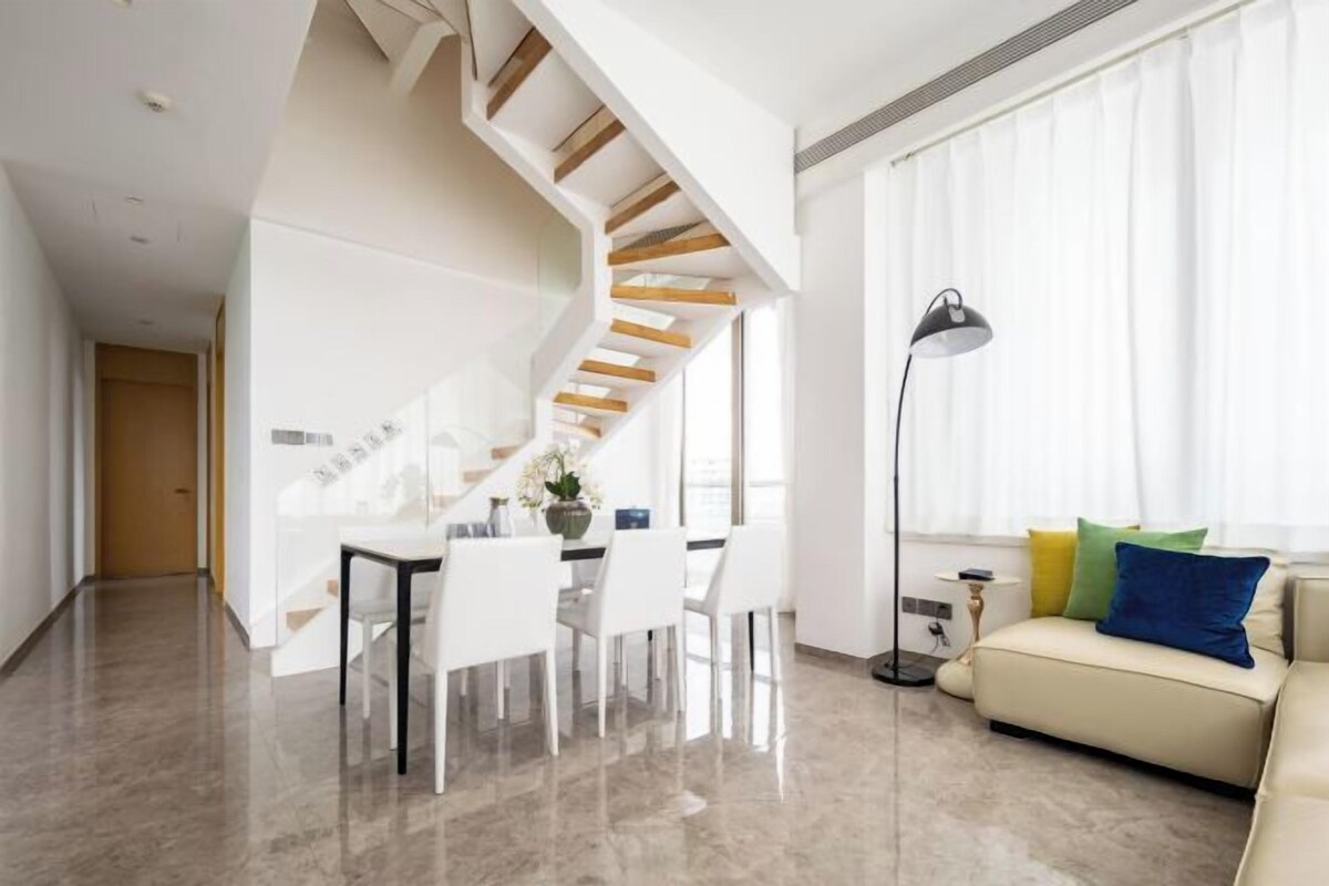 A modern living room with a staircase, a dining area, and a sofa with colorful cushions.