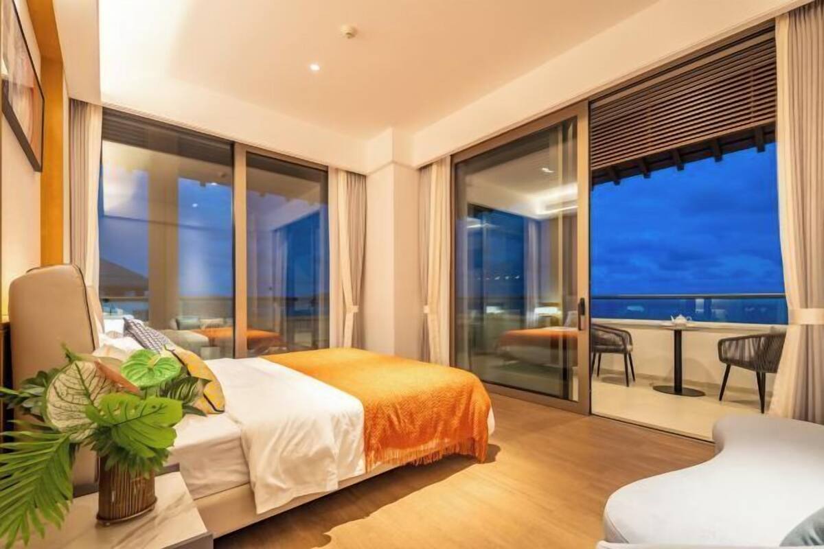 Une chambre d’hôtel comprenant un lit, un bureau avec une chaise, une plante en pot et un balcon avec des meubles d’extérieur.