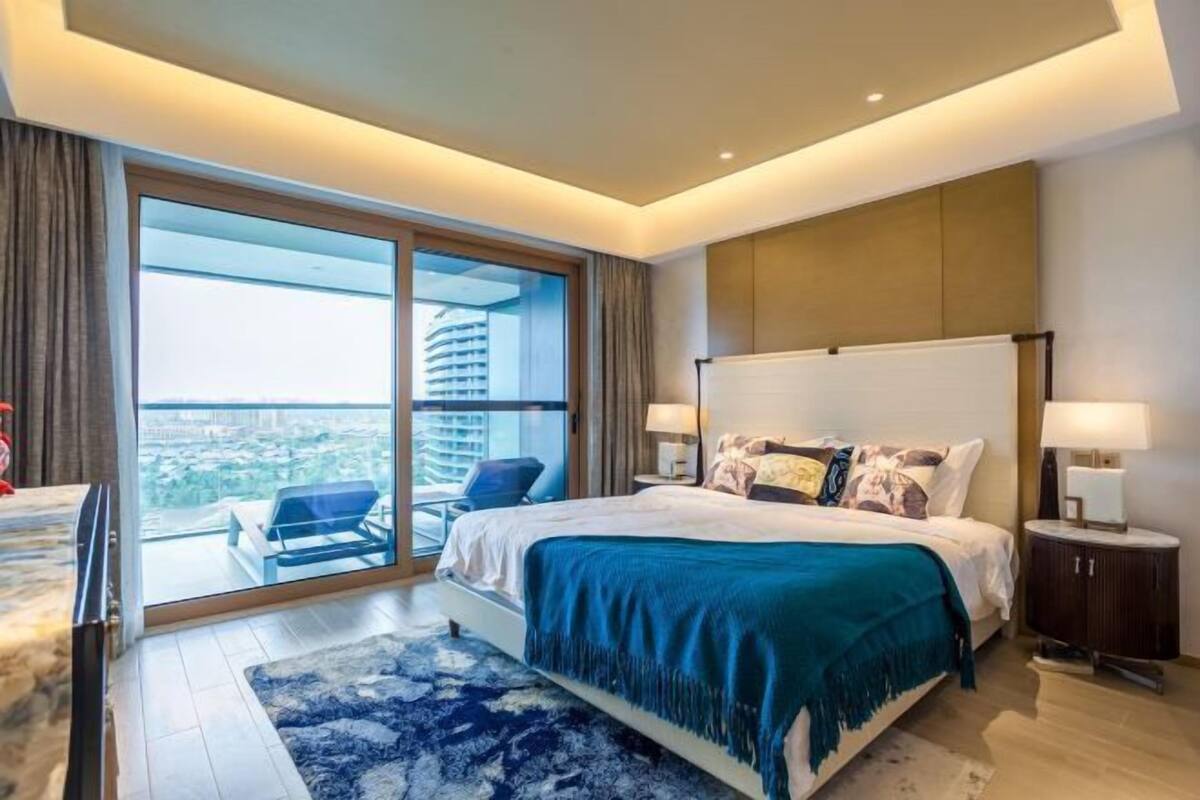 Une chambre d’hôtel moderne dotée d’un grand lit, d’un balcon offrant une vue sur la ville et d’un bureau avec une chaise.