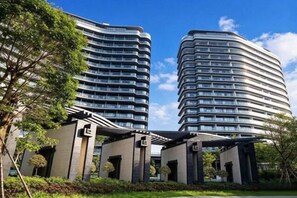 Two modern high-rise buildings with a curved facade, surrounded by greenery and a clear sky. - Jti seaview resort (Lingshui)