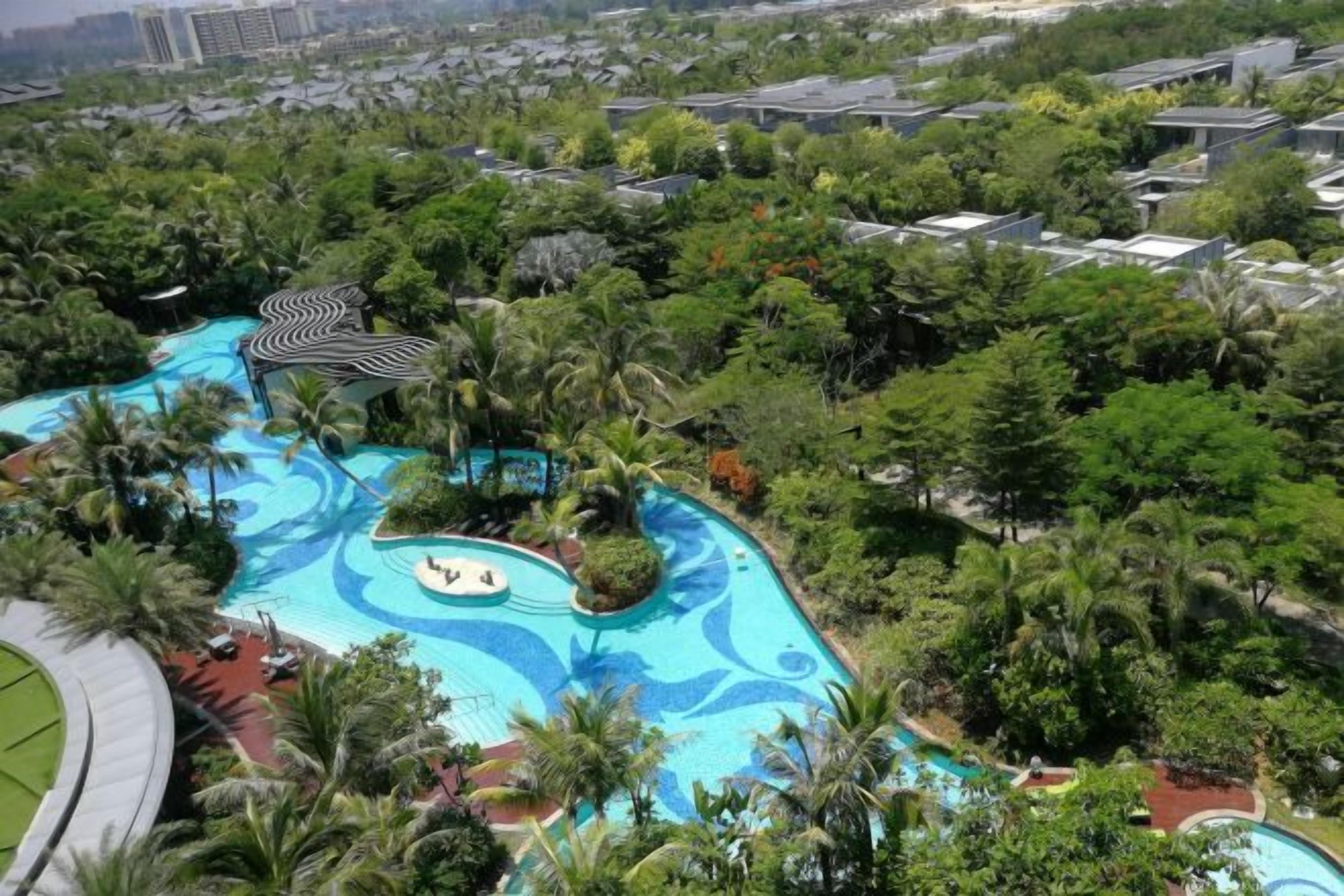 A resort with a large swimming pool surrounded by lush greenery and palm trees.