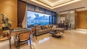 A modern living room with a sofa, coffee table, and dining area, featuring a large window with a view. - Haitang Bay Hongtai Seaview Holiday Apartment (Lingshui)