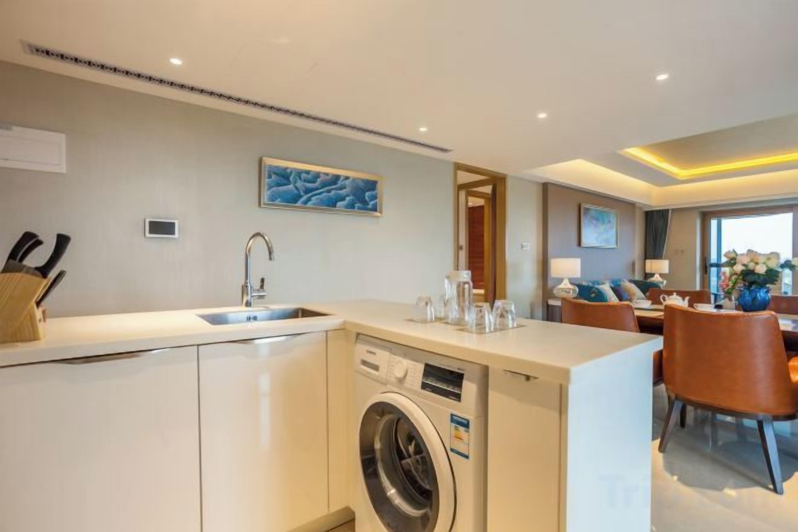 A modern kitchen with a built-in washing machine, a dining area with a table and chairs, and a large window providing natural light.