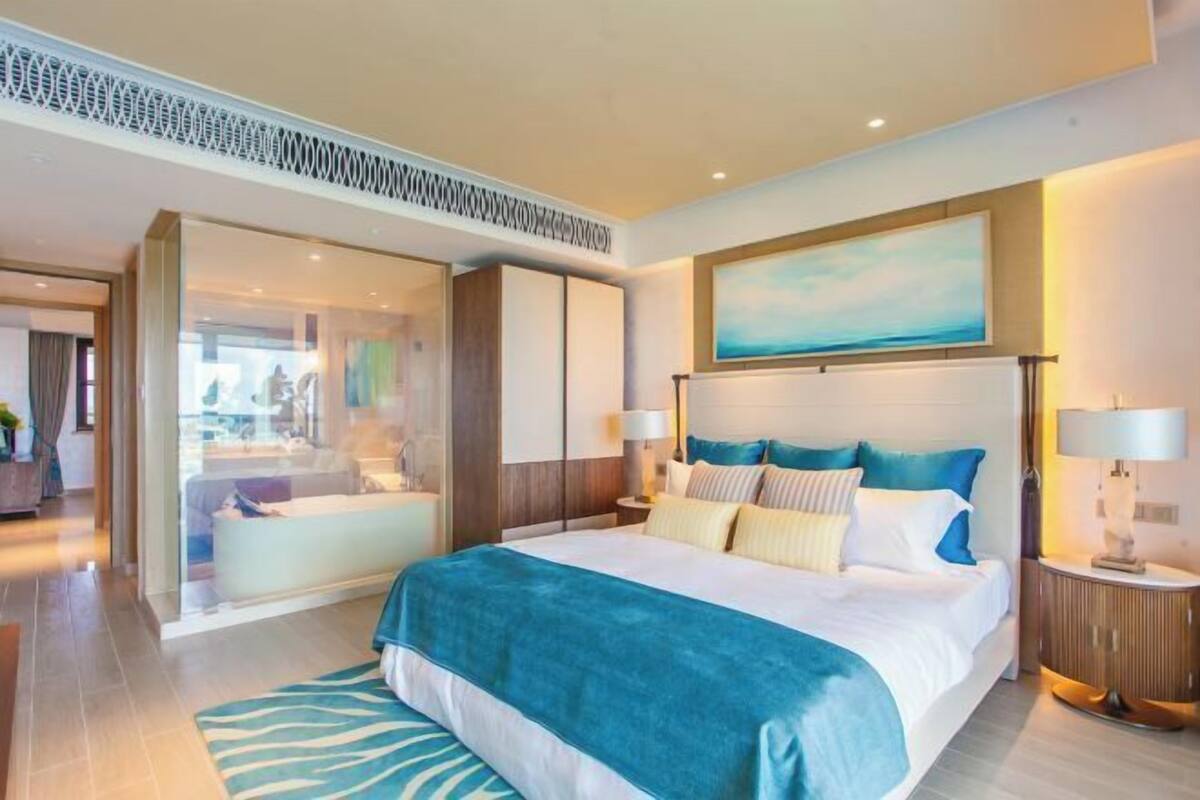 Une chambre d’hôtel moderne avec un grand lit, une cloison en verre, une vue sur la ville et un tableau au-dessus du lit.