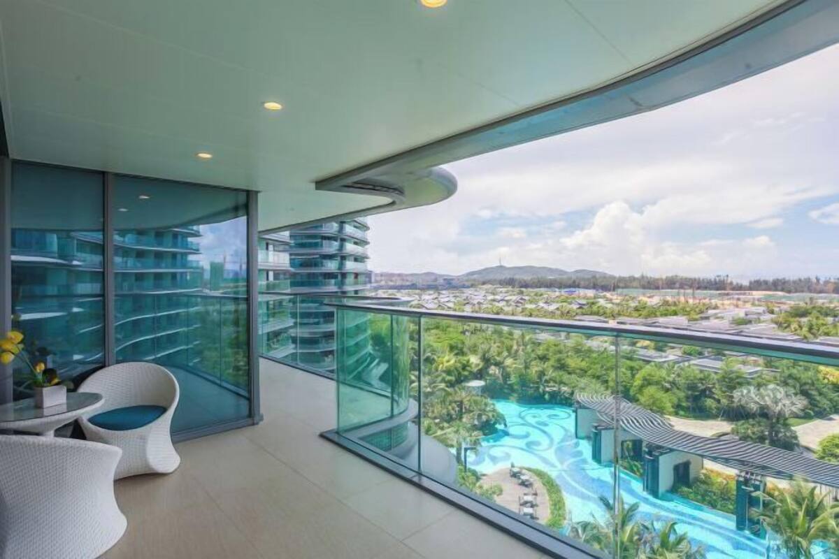 Un balcon moderne d’hôtel, doté d’une rambarde en verre, offrant une vue sur une piscine aménagée et la végétation environnante.