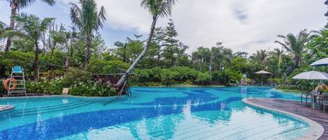 A swimming pool with a wooden deck, surrounded by palm trees and greenery.