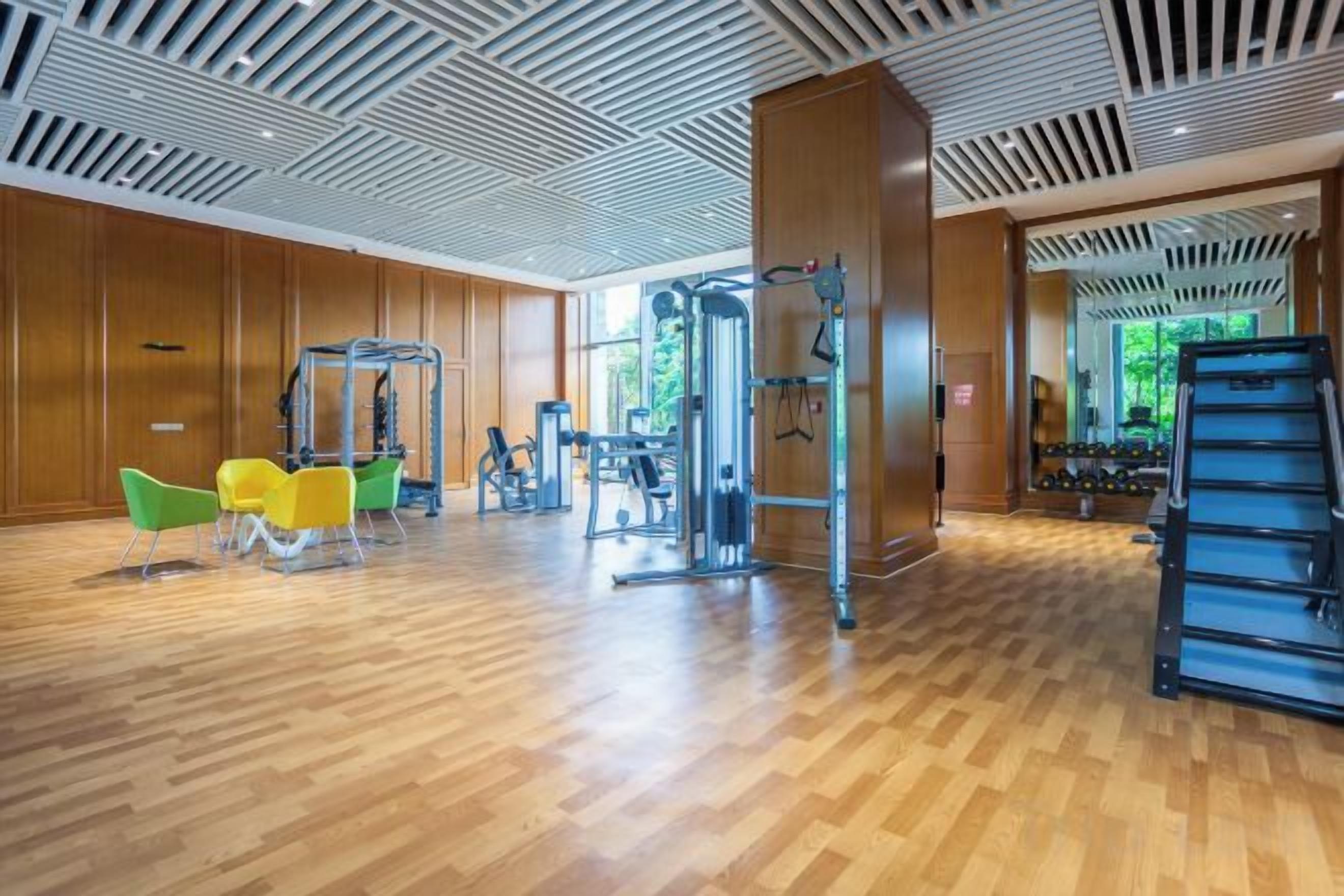 Un gimnasio con equipo de ejercicio, suelos de madera y ventanas amplias.