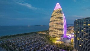 A modern hotel with a unique curved architecture, located near a coastal area with a view of the sea. - Haitang Bay Hongtai Seaview Holiday Apartment (Lingshui)