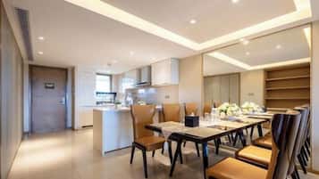 A modern dining area with a long table and chairs, a kitchen in the background, and a view of the city.