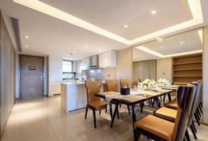 A modern dining area with a long table and chairs, a kitchen in the background, and a view of the city. - Jti seaview resort (Lingshui)