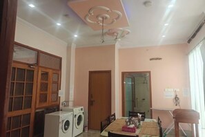 A room with a washing machine, a table with chairs, a ceiling light fixture, and a door.
