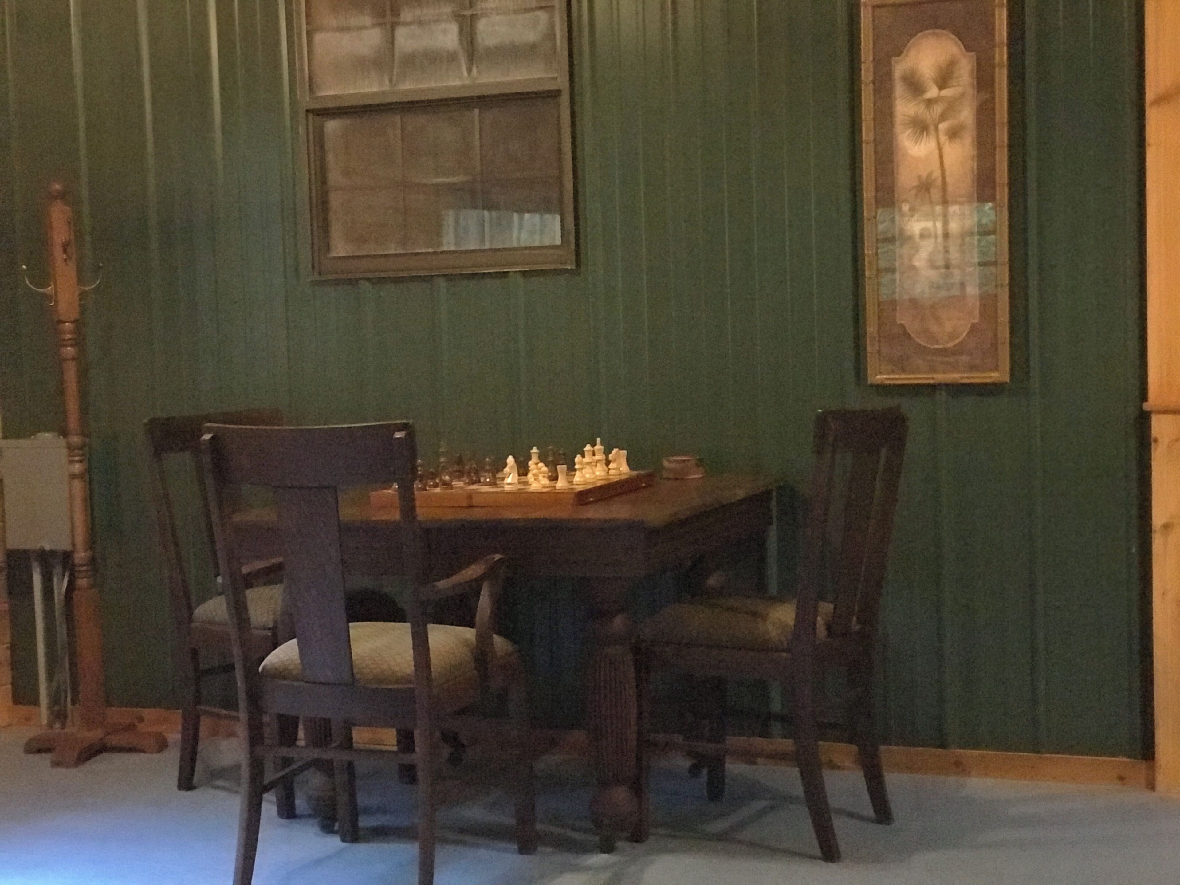 A dining area with a wooden table and chairs, a chessboard, and a framed picture on the wall.