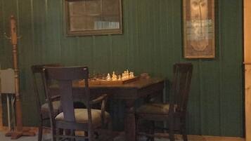 A dining area with a wooden table and chairs, a chessboard, and a framed picture on the wall.