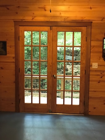 A wooden double door with a grid pattern, leading to an outdoor area with a wooden deck and greenery.