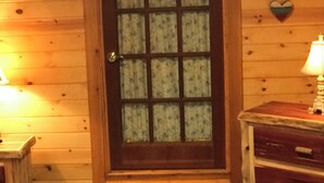A wooden door with a glass panel, a heart-shaped decoration on the wall, and a lamp on a wooden table.