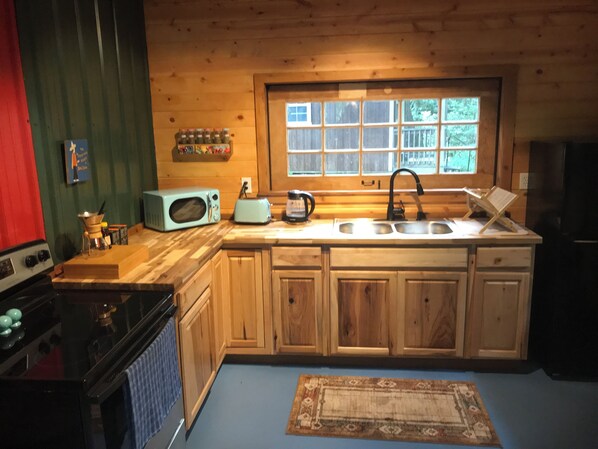 Una cocina con armarios de madera, microondas, tostadora, lavaplatos y una ventana con vistas a árboles.