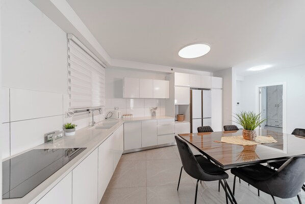 A modern kitchen with white cabinetry, a black countertop, and a dining area with a glass table and black chairs.