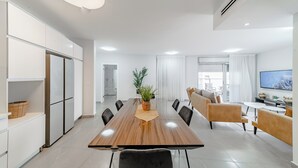 Una sala de estar moderna con una mesa de comedor de madera, asientos cómodos, un televisor y un amplio ventanal.