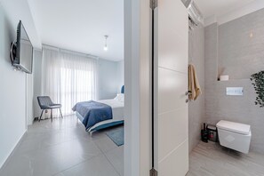 A modern hotel room with a bed, a chair, a TV, and a shower area.