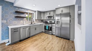A modern kitchen with grey cabinets, stainless steel appliances, and a patterned backsplash. - Bermuda Palms: Pool, Spa, Arcade Game, Fire pit! (Bermuda Dunes)