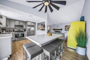Una cocina moderna con una isla central, taburetes de bar y un ventilador de techo.