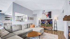 A modern living room with a grey sectional sofa, a coffee table, a flat-screen TV, and a fireplace. - Bermuda Palms: Pool, Spa, Arcade Game, Fire pit! (Bermuda Dunes)