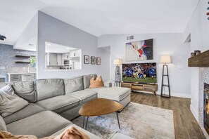 Una sala moderna con un sofá seccional, una mesa de centro, un televisor de pantalla plana y una chimenea.