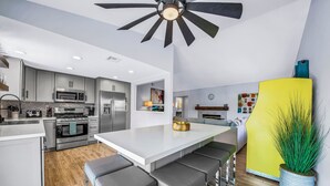 A modern kitchen with a central island, stainless steel appliances, and a ceiling fan. - Bermuda Palms: Pool, Spa, Arcade Game, Fire pit! (Bermuda Dunes)