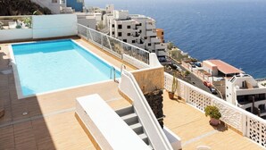 Ein Pool auf dem Dach mit freiem Blick auf das Meer, eine weiße Treppe und ein kleiner Tisch mit Stühlen.