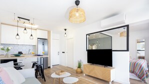 Eine moderne Wohnung mit Küche, Essbereich und Wohnzimmer. Sie umfasst einen Fernseher, eine Couch, einen Esstisch und eine kleine Kücheninsel.