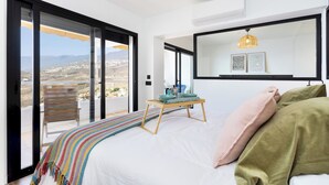 Ein Schlafzimmer mit einem großen Bett, einem Nachttisch, einem Stuhl und Blick auf die Landschaft durch große Fenster.