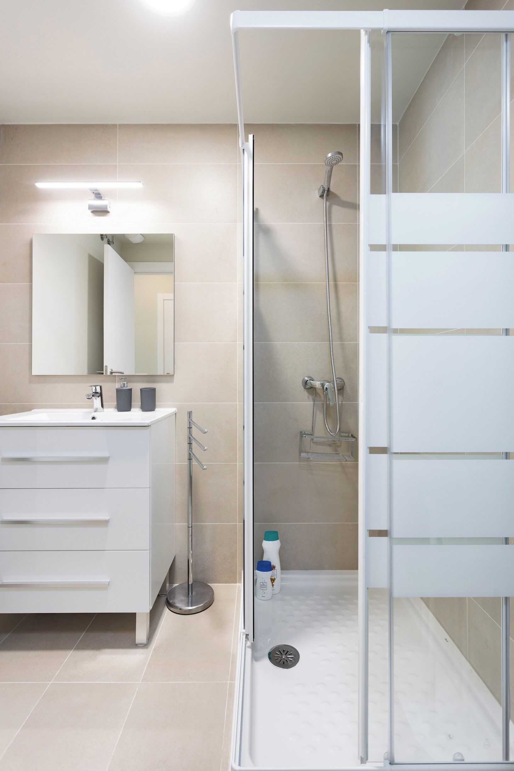 A modern bathroom with a white vanity, a large mirror, a shower enclosure, and a toilet.