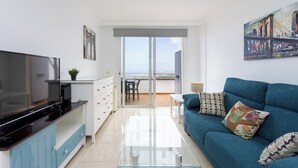 A modern living room with a flat-screen TV, a blue sofa, and a balcony with a city view. - Home2Book Sunset Apt Costa Adeje, Pool & Terrace (Adeje)