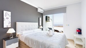 A modern bedroom with a large bed, a nightstand, a bedside table, and a view of the outdoors through a sliding door. - Home2Book Sunset Apt Costa Adeje, Pool & Terrace (Adeje)