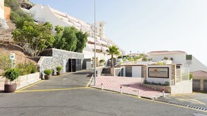 A hotel entrance with a stone wall, potted plants, and a sign reading "The Sunset". - Home2Book Sunset Apt Costa Adeje, Pool & Terrace (Adeje)