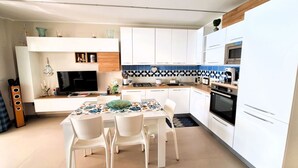A modern kitchen with white cabinets, a tiled backsplash, and a dining area with white chairs and a table.