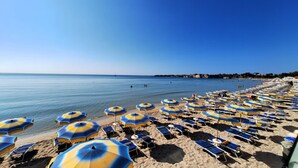 A beach with rows of sun loungers and umbrellas, a clear blue sky, and calm sea.
