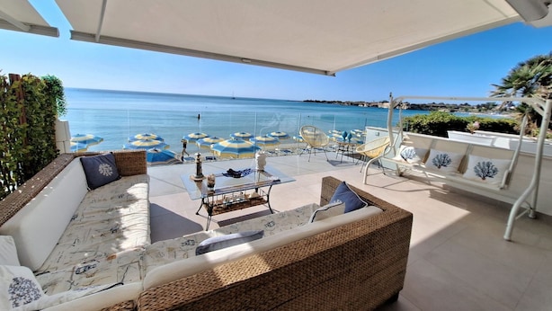 A sunlit outdoor seating area with wicker furniture, a glass table, and blue and white umbrellas.