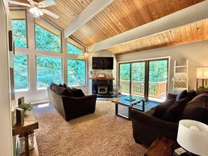 A spacious living room with large windows, a fireplace, and a ceiling fan.
