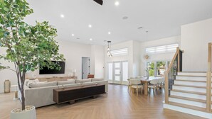 A spacious living room with a large sofa, a coffee table, and a dining area with a table and chairs. There is a staircase leading to another level.