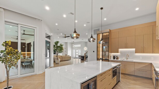 A modern kitchen with a large island, wooden cabinets, and pendant lighting.