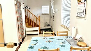 Un coin repas avec une table recouverte d’une nappe bleue à motifs de forêt, des chaises en bois et un banc en bois.
