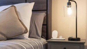 Un lit bien fait, avec une literie à rayures et deux oreillers, une table de chevet avec une lampe, et un petit objet blanc posé sur la table.