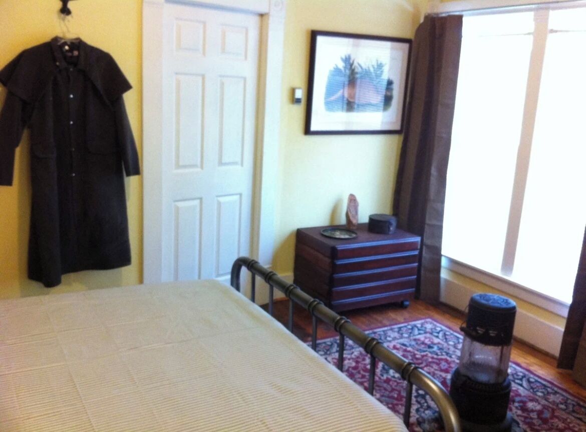 A bedroom with a bed, a dresser, a coat rack, and a window with curtains.